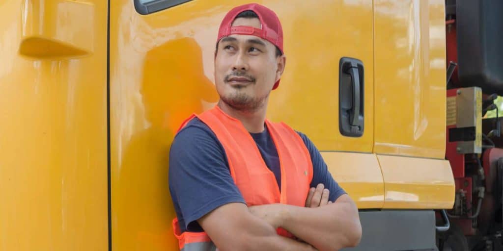 A trucker standing in front of a semi-truck with his arms crossed as he gets the most out of his CDL training