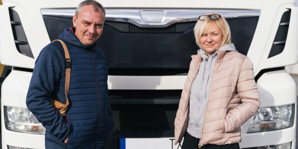 A husband-and-wife team trucking team in front of a white semi