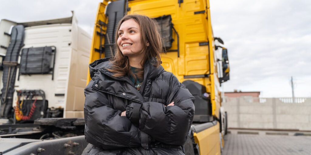 A woman in trucking next to a yellow semi-truck