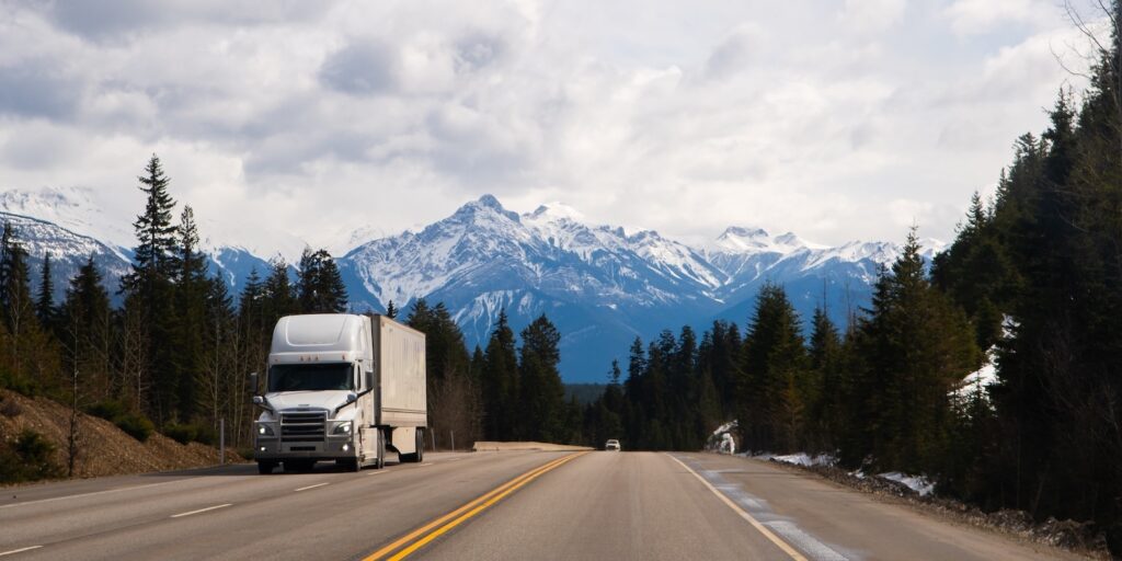 A white semi-truck on a highway with mountains in the background