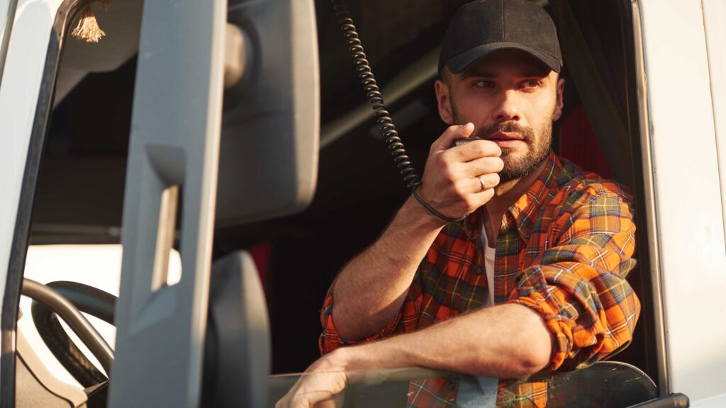Truck driver in plaid shirt using a radio microphone while sitting in the cab.